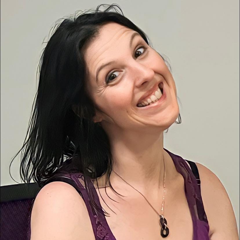 Portrait d’une femme souriante en haut débardeur violet, regard penché vers la caméra.